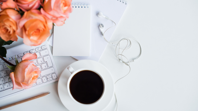 Orange roses, notepad, pen, headphones, cup of coffee and a keyboard on top of a while desk top. 3 Reasons Why Twitter Is My Blogs Best Friend